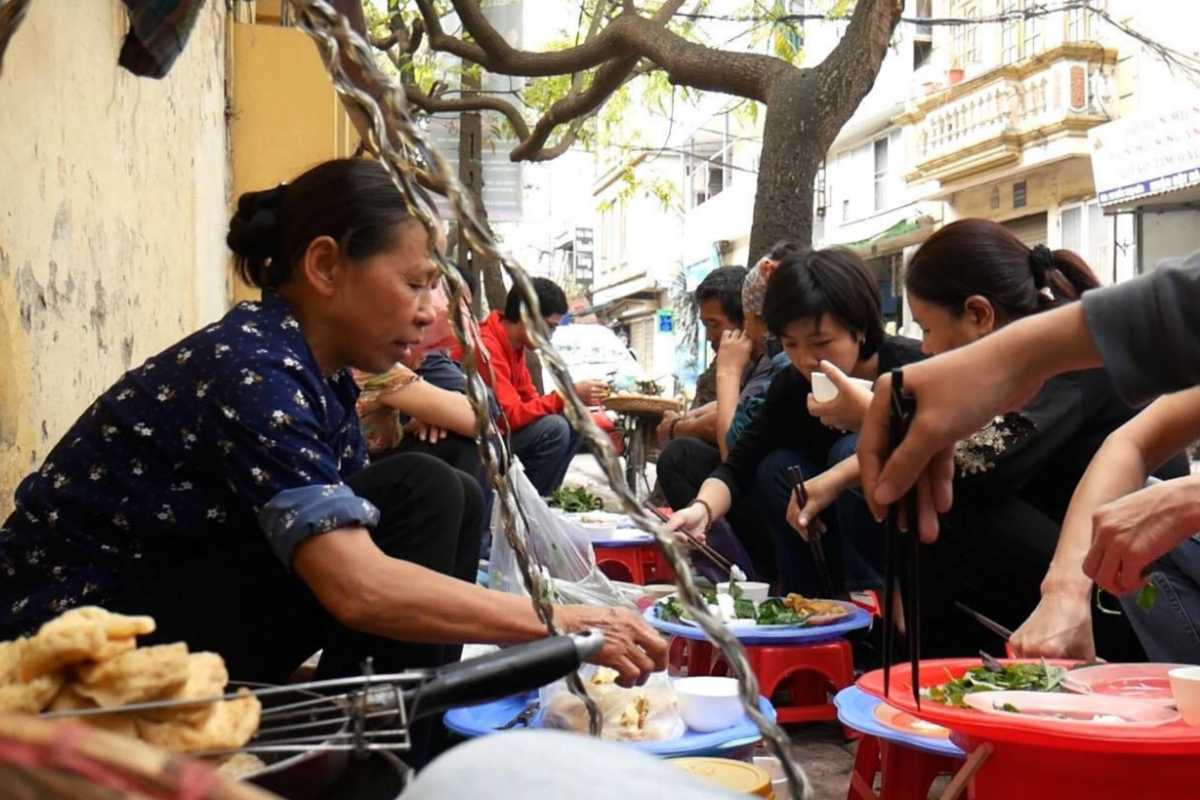 The sidewalk setting with low tables and stools reflects Hanoi’s style